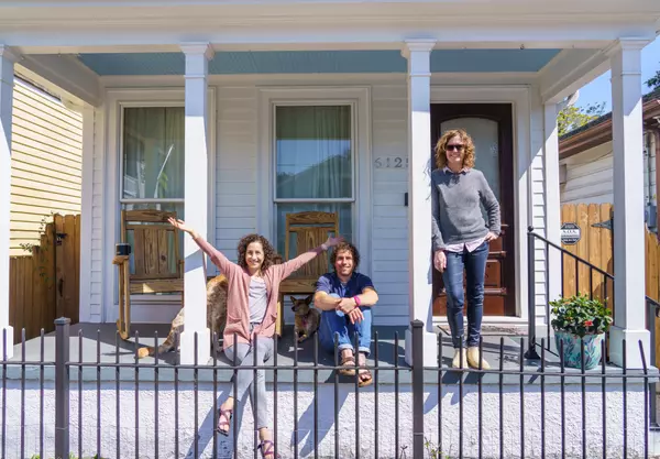 A man and woman celebrate on the front porch of their new home while Tracey Moore stands nearby