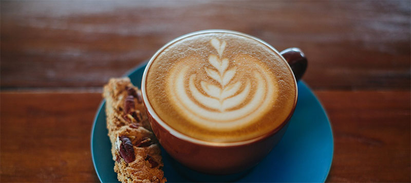 A perfect latte with heart-shaped foam served with biscotti at Sip! on the Square