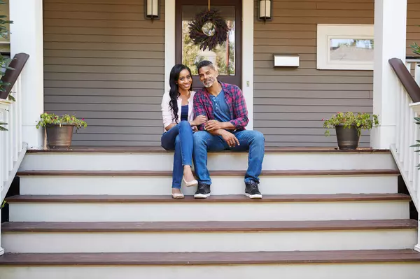 couple-sitting-on-steps-leading-up-to-porch-of-home