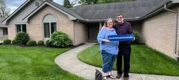 Two clients in front of a new house with a "JUSTBOUGHTAHOUSE" sign