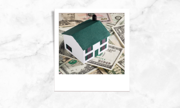 Photo of a house block standing above some paper bills