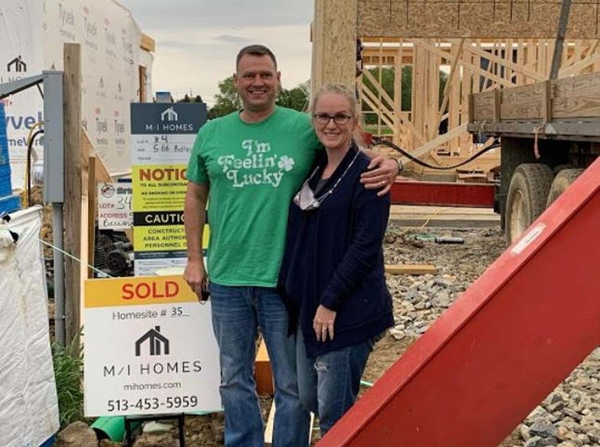 Happy couple smiling in front of home construction site.