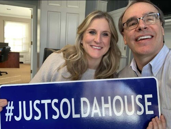 Woman smiling and holding a hashtag Just Sold A House Sign next to David Campbell.