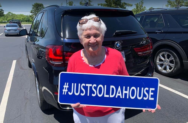 Happy client smiling and holding a sign that says hashtag just sold a house.