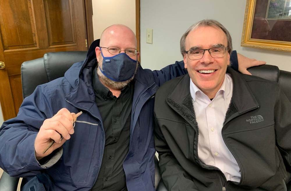 Happy client holding a house key while wearing a mask next to David Campbell.