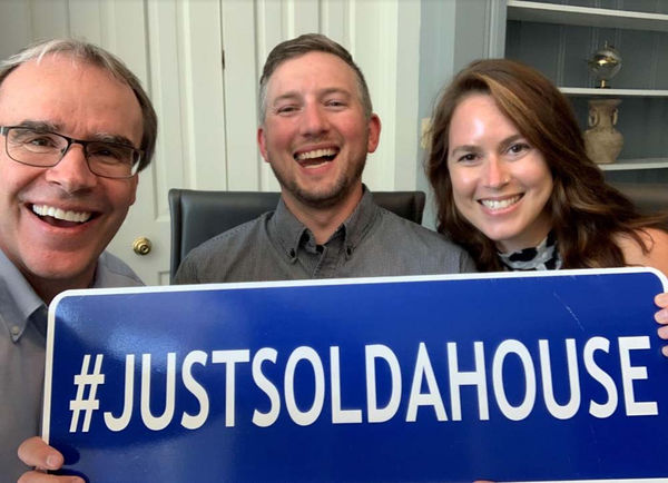 Happy couple holding an sign that says hashtag just sold a house next to David Campbell.