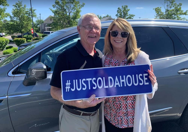 Happy client holding a sign that says hashtag just sold a house and smiling.