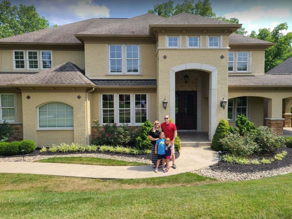 Happy family smiling in front of large house.