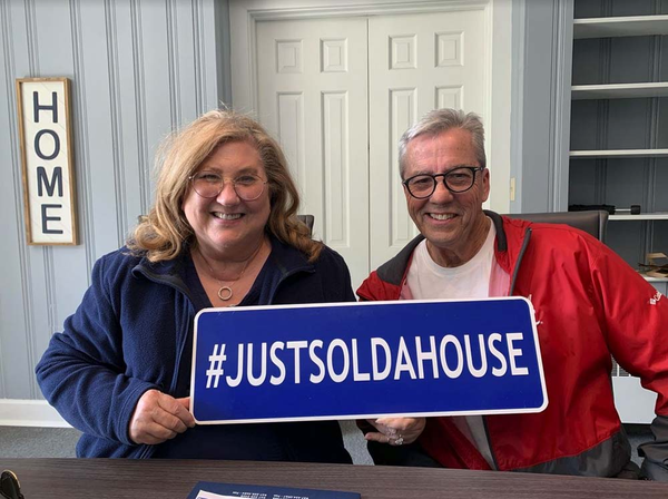 Happy clients holding a sign that reads hashtag just sold a house.