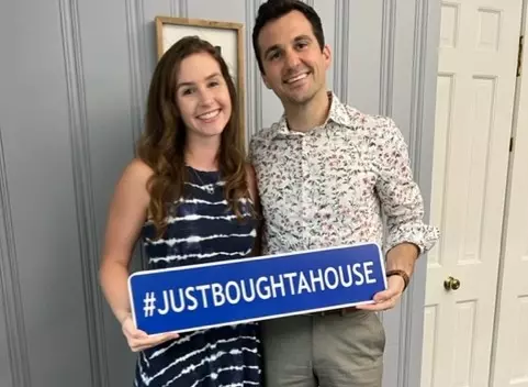 Couple holding "#JUSTBOUGHTAHOUSE" sign