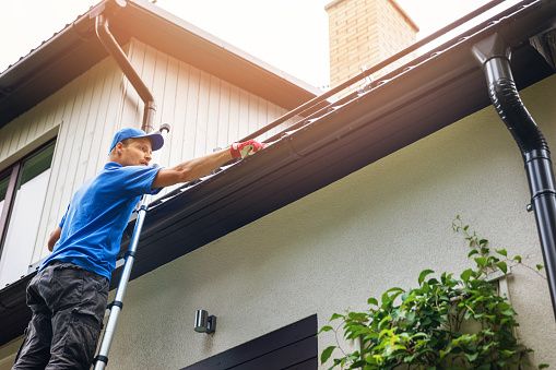 man on ladder cleaning gutters on a house 