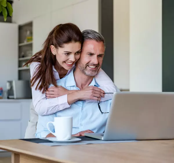 happy-couple-at-table-at-home-sharing-a-laptop-2022-12-16-22-29-00-utc (1)