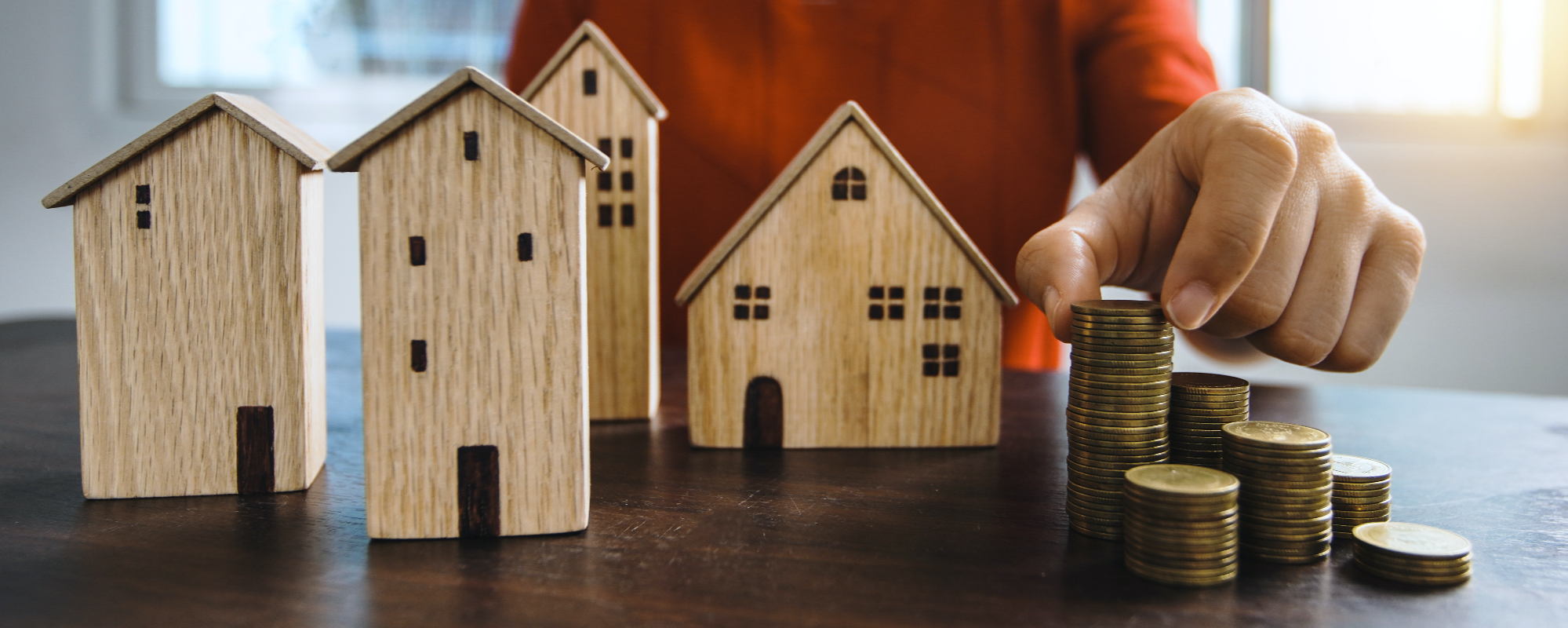 Wooden model homes on a table with a stack of coins