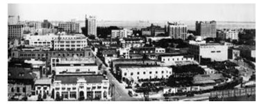 Historic black and white photograph of Miami in the early 20th century, showcasing the burgeoning cityscape with vintage cars on bustling streets and early architectural marvels under the radiant Miami sun