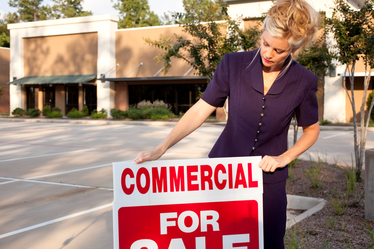 Real estate professional posting for sale sign in front of commercial listing