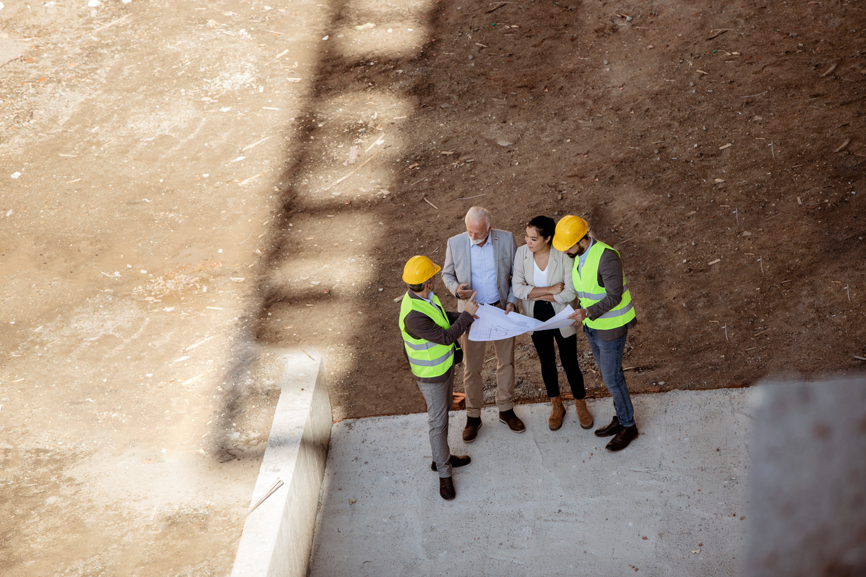 Engineers and construction workers at real estate development site reviewing plans