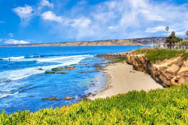 Scenic La Jolla Cove coastline in San Diego featuring clear blue water, sandy beach, and oceanfront real estate, Realtor Betty Torano.