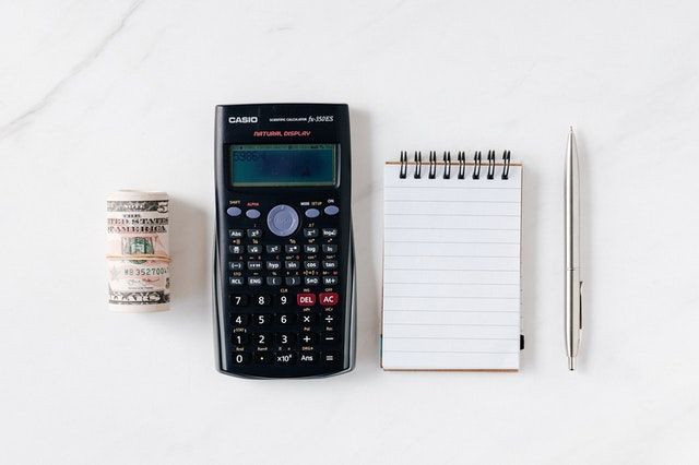 Rolled up banknotes, a calculator, a notebook, and a pen.