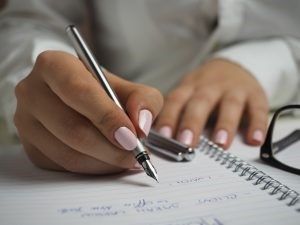 A girl with baby pink nail polish writing a list in her notebook. 