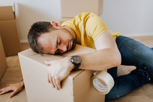 A man hugging a box he is securing with duct tape.