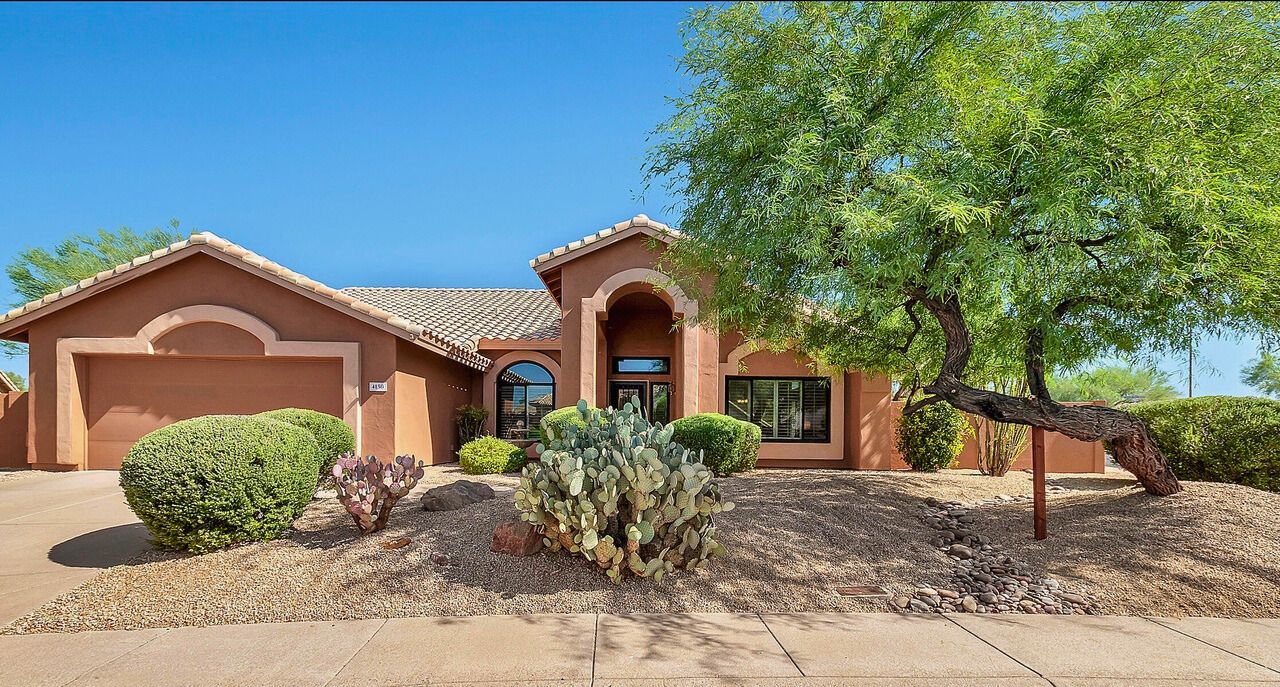 Exterior view of a beautiful single-story home in Tatum Ranch, Cave Creek, AZ, featuring a well-maintained front yard, modern design with light-colored stucco, large windows, and a spacious corner lot surrounded by desert landscaping.