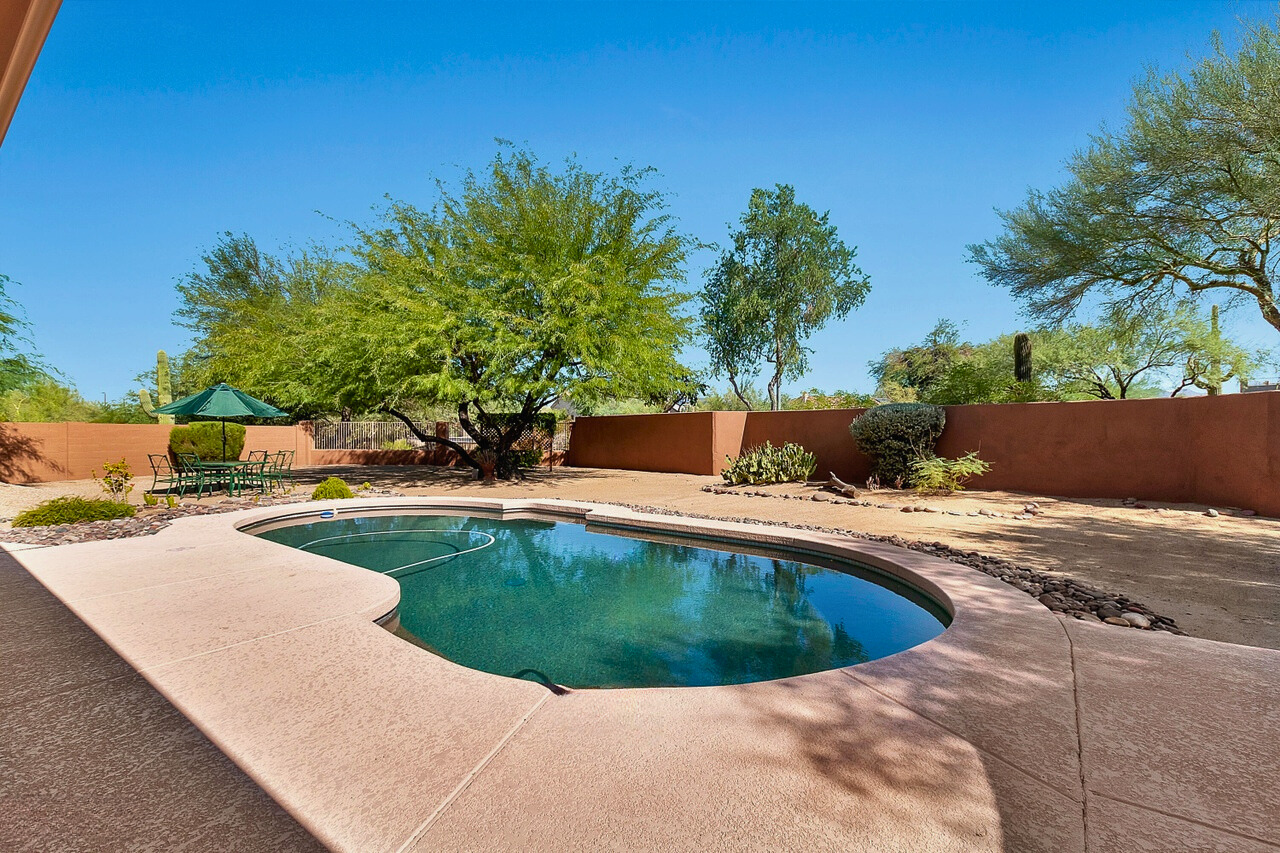 Spacious backyard of a Tatum Ranch home in Cave Creek, AZ, featuring a large pool surrounded by desert landscaping, with plenty of room for outdoor seating, a fire pit, and additional amenities, creating the perfect space for relaxing or entertaining in the Arizona sun.