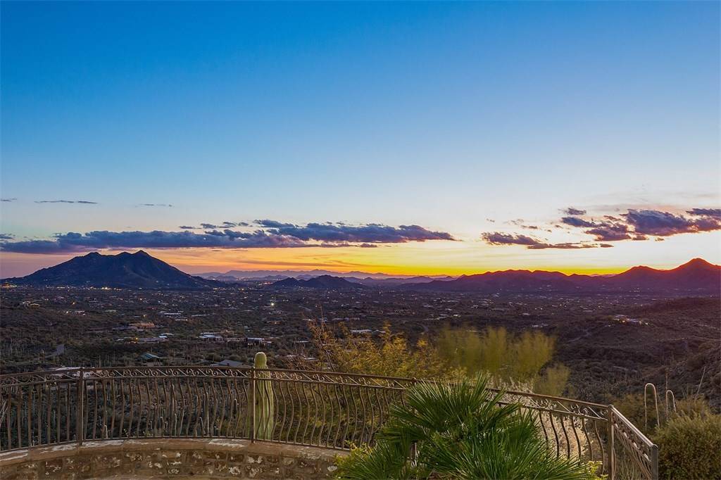 A breathtaking view overlooking the desert landscape of Cave Creek, AZ at sunset, with vibrant hues of orange, pink, and purple illuminating the sky, silhouetting the rugged mountains and cacti below, capturing the serene beauty of the Sonoran Desert.