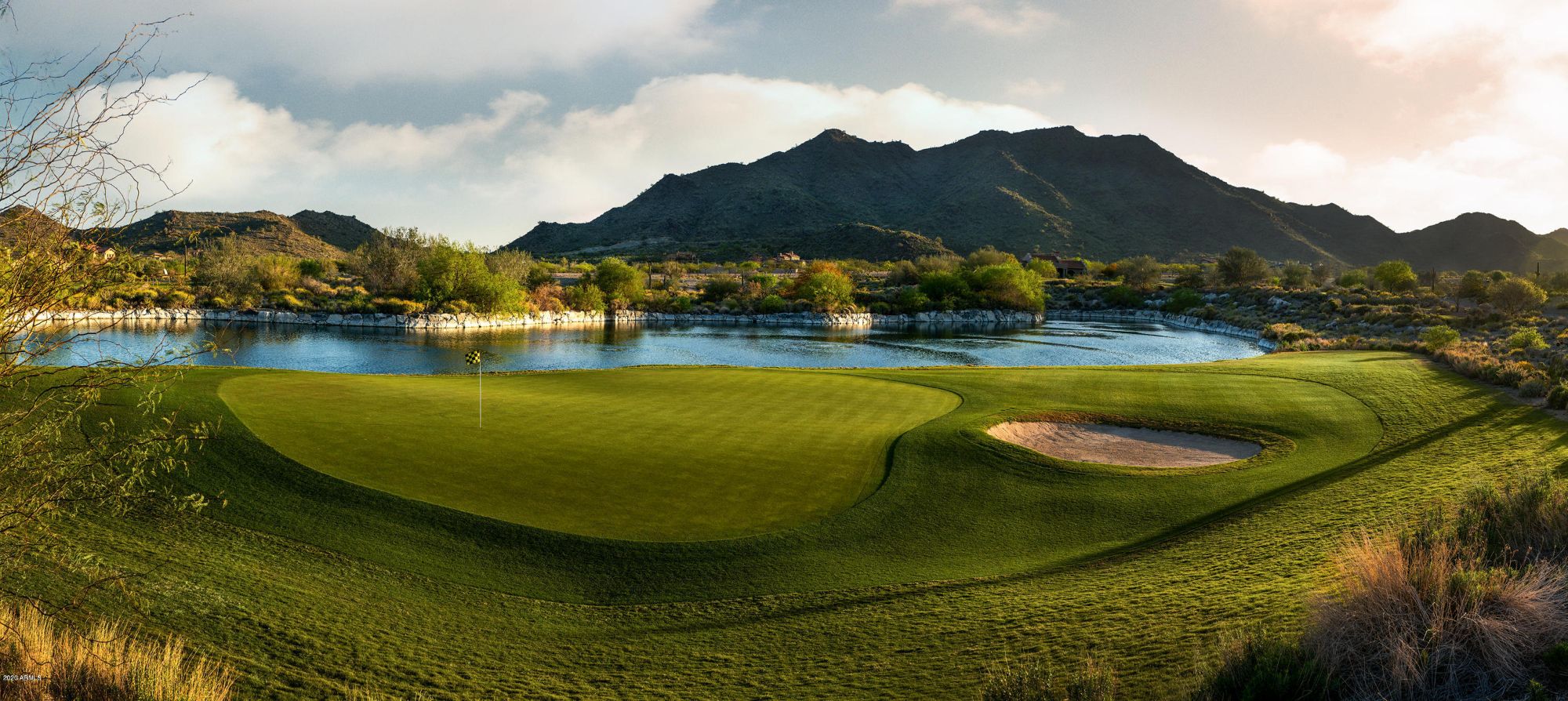 Scenic view of the Founders Course at Verrado Golf Club in Buckeye, Arizona, featuring lush greens, water hazards, and a mountainous desert backdrop, showcasing the premier golfing experience within this master-planned community.