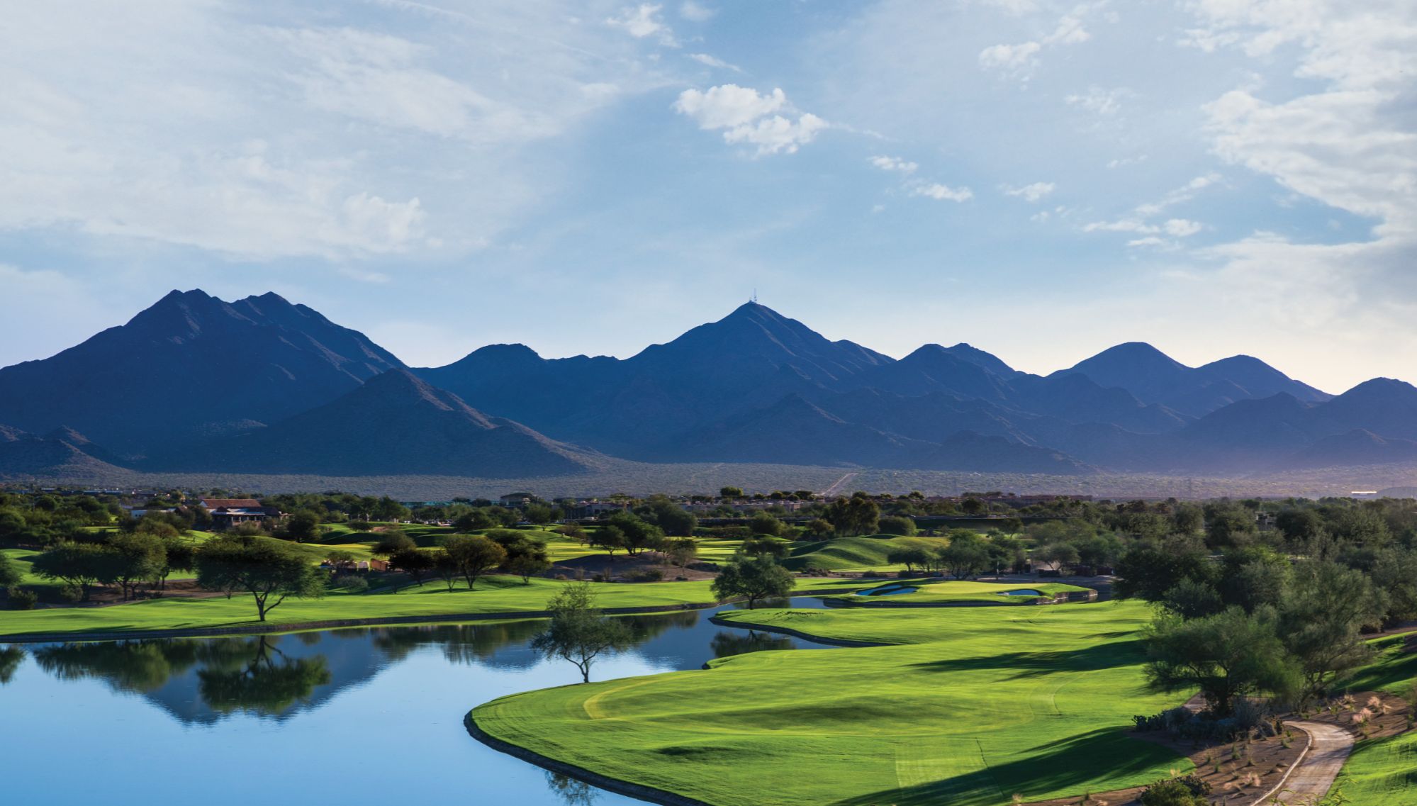 Scenic view of the TPC Scottsdale golf course in Scottsdale, Arizona, showcasing the lush green fairways, water features, and the stunning McDowell Mountains in the background under a clear blue sky.