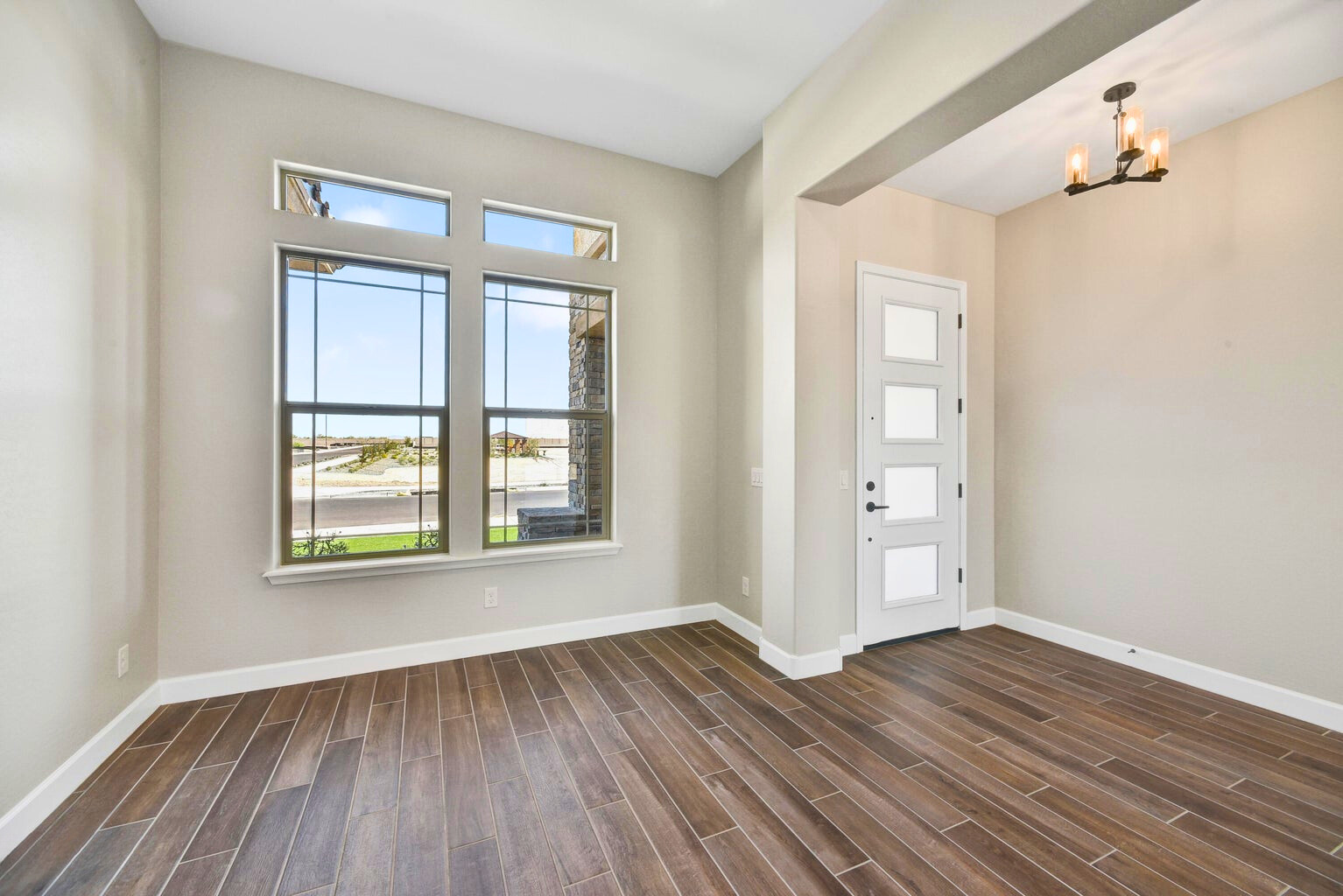 Grand entrance of a new build home in Sentiero at Windrose, Waddell, AZ, featuring high ceilings, large windows allowing natural light, elegant wood-look tile flooring, and a modern front door. The spacious entryway creates a welcoming atmosphere in this luxury home by David Weekley Homes.