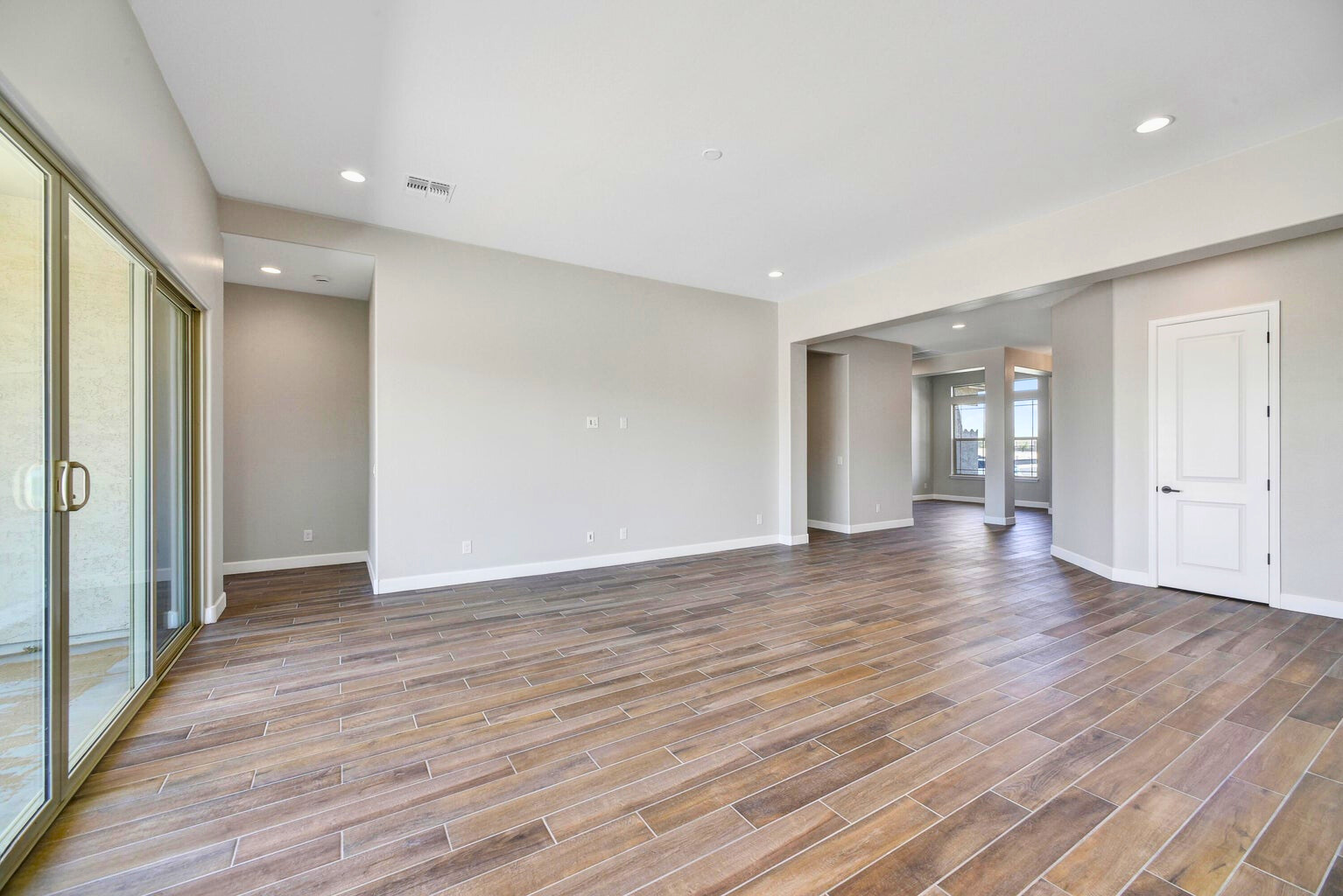 Spacious living areas in this new construction home in Sentiero at Windrose, Waddell, AZ, featuring elegant wood-look tile flooring, high ceilings, and a seamless transition to the outdoor patio through large sliding glass doors. This open-concept layout is perfect for both family living and entertaining.