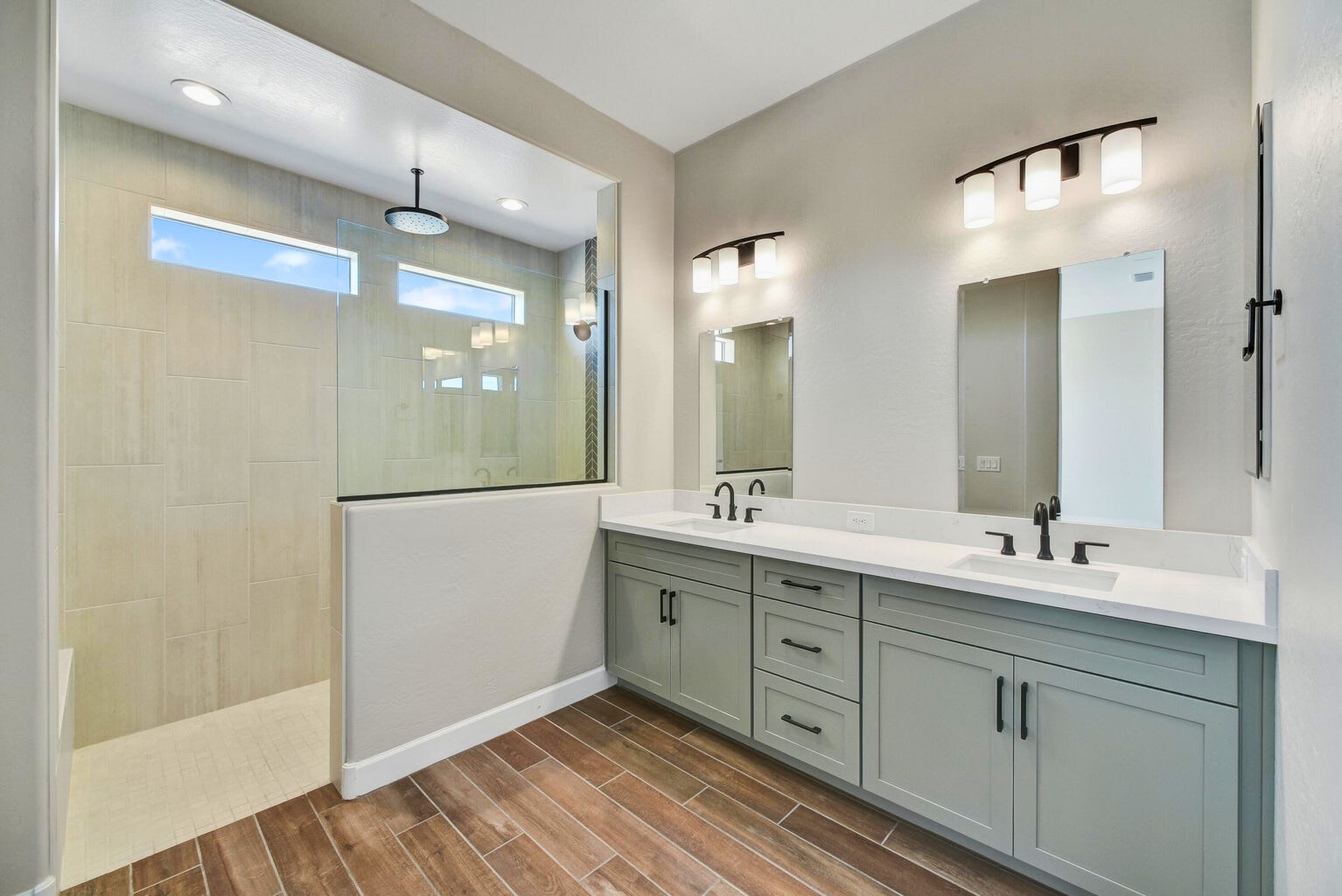 Luxurious owner's retreat bathroom in a new construction home in Sentiero at Windrose, Waddell, AZ, featuring a spacious walk-in shower with modern rain showerhead, double vanity with quartz countertops, custom cabinetry, and elegant lighting. The sleek design and premium finishes create a spa-like atmosphere in this serene space.