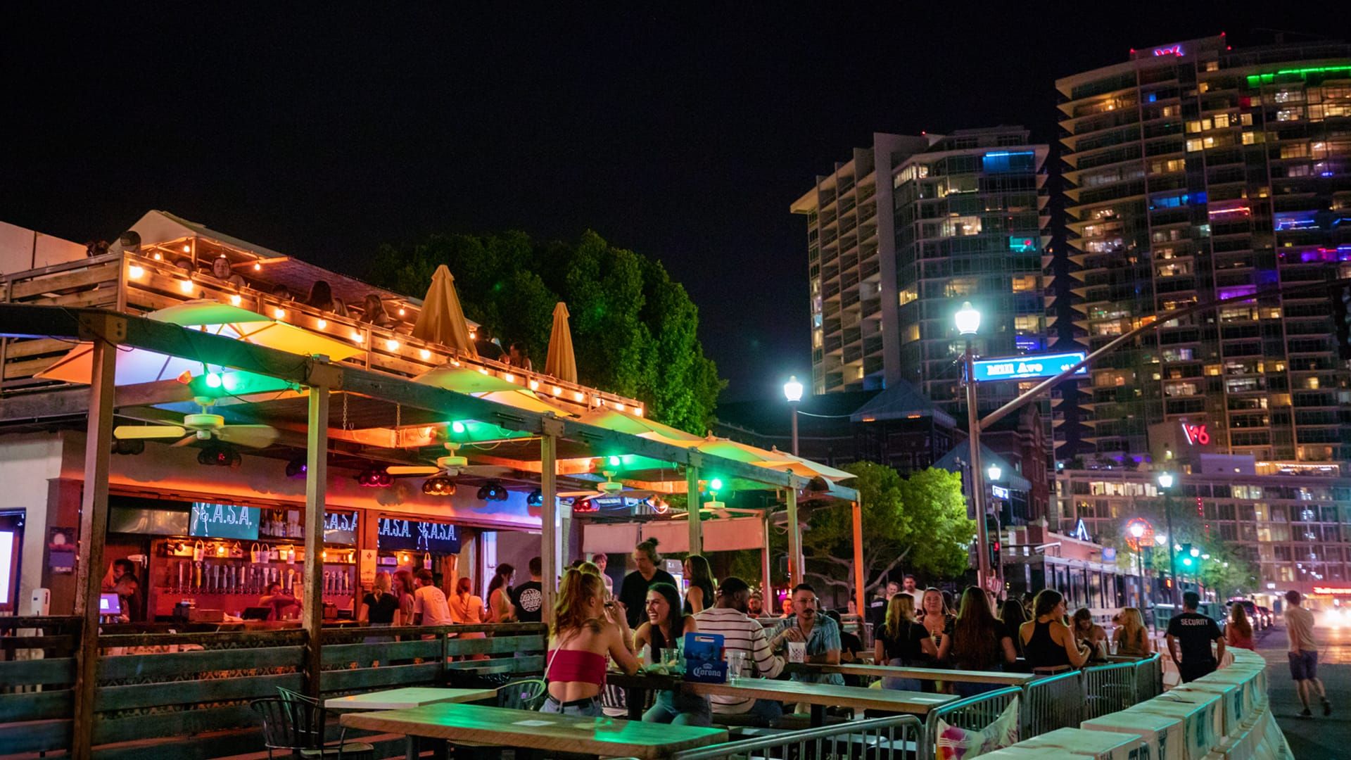 Vibrant nightlife scene in Tempe, Arizona, with a lively outdoor bar, illuminated seating area, and people enjoying the evening atmosphere on Mill Avenue, showcasing Tempe's bustling nightlife and urban entertainment.