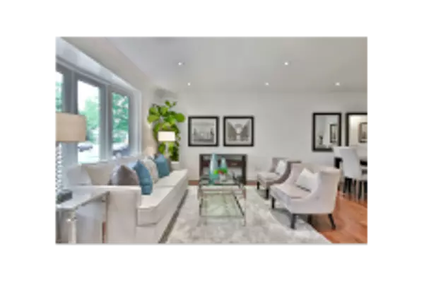 Elegant living room with a white sofa, plush armchairs, a glass coffee table, and decorative accents, with large windows in real estate