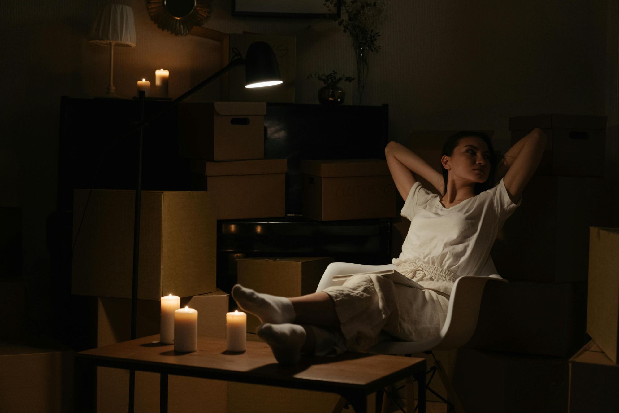 A girl relaxing in her new home at night, sitting comfortably among unpacked moving boxes, with soft lighting creating a cozy atmosphere