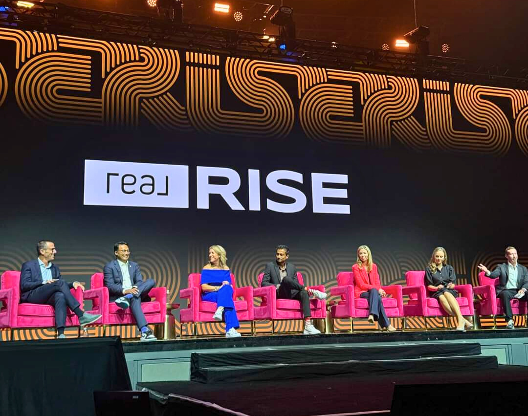 Panel of Real Broker leaders and industry experts on stage at the 2024 Real Broker RISE Conference in Las Vegas, showcasing the latest announcements and innovations in real estate technology, networking opportunities, and strategies to enhance agent success, with vibrant branding and energy reflecting the event's impactful agenda.