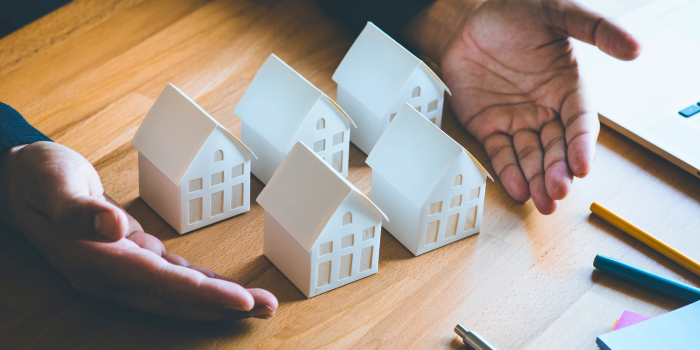 Investor’s hands surrounding miniature houses on a desk, symbolizing strategic decision-making in the real estate market. Highlights how real estate investors assess election impacts cautiously, focusing on long-term gains and market fundamentals rather than political cycles