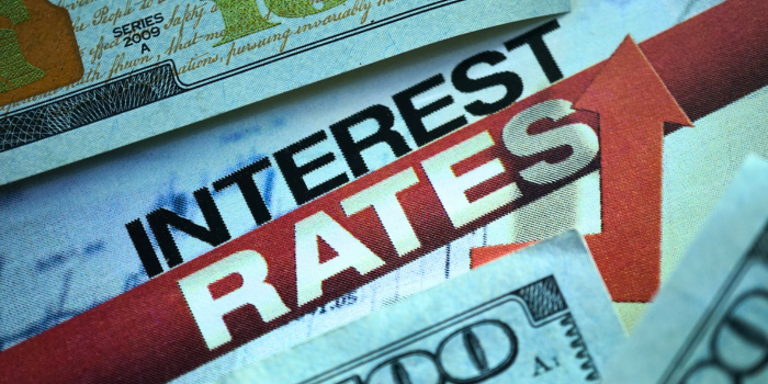 Close-up of the words 'Interest Rates' with dollar bills and an upward arrow, symbolizing the influence of mortgage rates and Federal Reserve policies on the housing market. Emphasizes how changes in interest rates can significantly impact housing affordability, buyer demand, and real estate investment strategies.