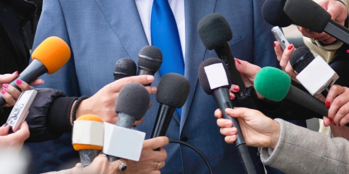 Close-up of a public figure surrounded by journalists with microphones, symbolizing the media’s role in influencing public perceptions. Highlights how political coverage, particularly around elections, can shape narratives on the housing market and impact consumer confidence in real estate decisions.