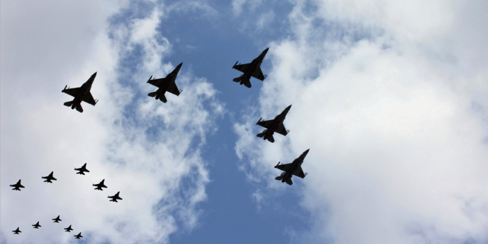 This image shows a formation of Air Force jets flying in perfect synchronization against a backdrop of a partly cloudy sky. The jets, likely F-16s or F-35s, are silhouetted against the sky as they soar over the area surrounding Luke Air Force Base in Arizona. The arrangement of the jets in different groupings demonstrates the precision and coordination typical of military air exercises. The scene captures both the power and grace of these advanced fighter aircraft as they perform maneuvers high above the desert landscape.