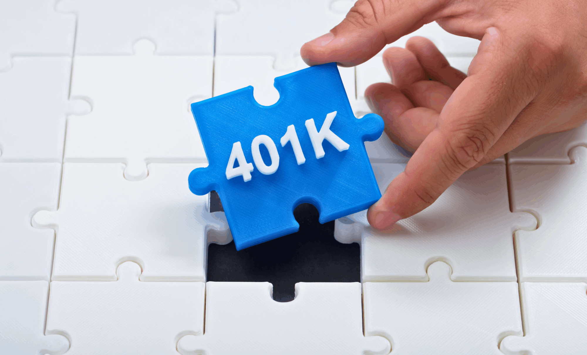 A hand holding a blue puzzle piece labeled '401K,' fitting it into a blank puzzle, symbolizing the role of Solo 401(k) plans for self-employed individuals and real estate professionals as a key component in retirement planning.