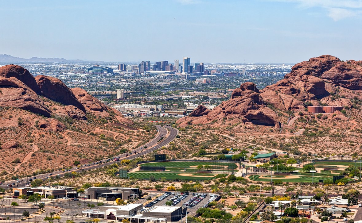 A stunning panoramic view of the Arizona desert, featuring rugged red rock formations with the Phoenix skyline in the distance. The image captures the natural beauty and urban vibrancy of the state, making it an ideal cover photo for a blog that educates military families on everything they need to know about moving to Arizona, including Luke Air Force Base. The combination of scenic landscapes and city life emphasizes the state's appeal to both military personnel and their families, providing valuable insight for those relocating to the area.