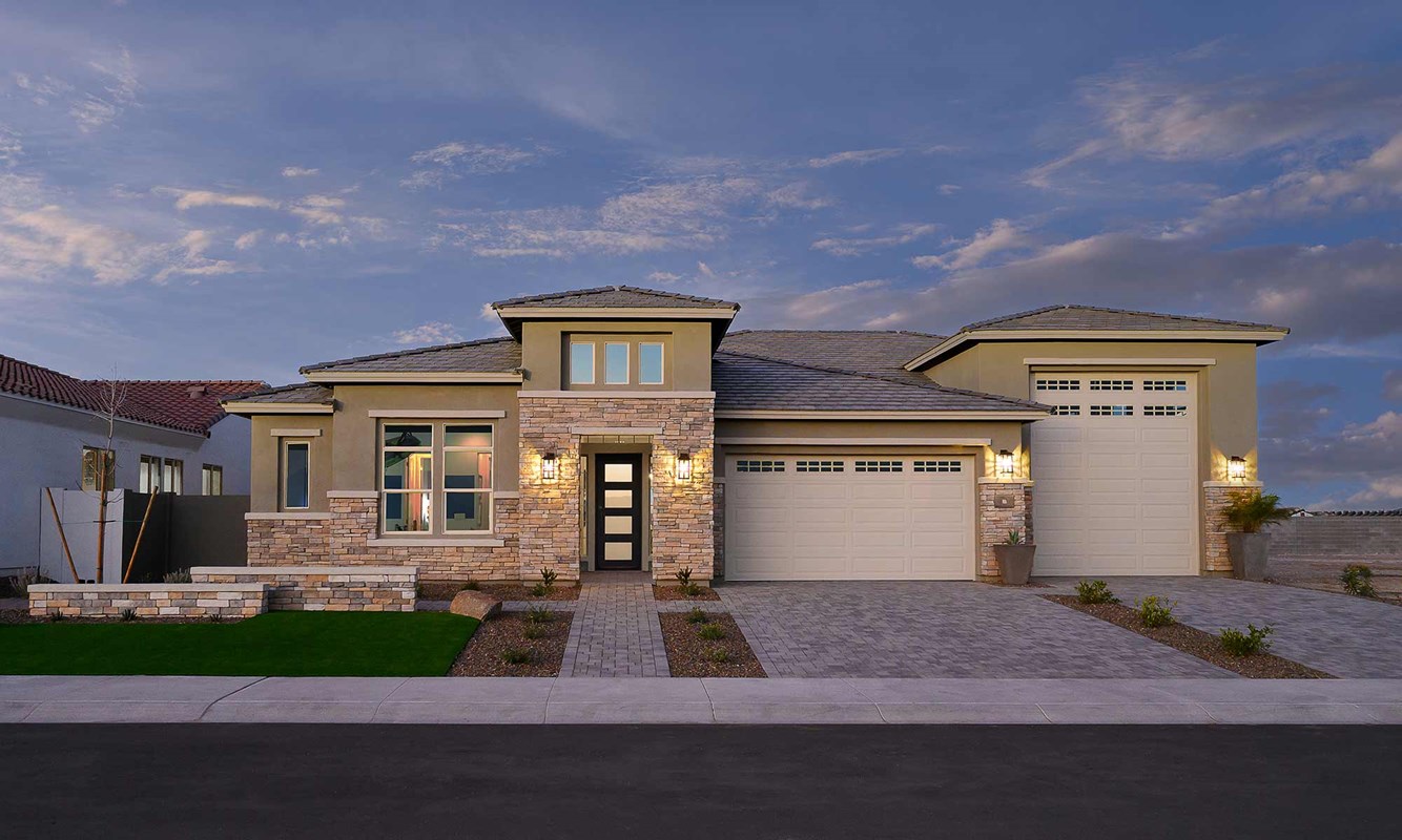 A modern, beautifully designed new home in Litchfield Park, AZ, featuring a stone-accented exterior with sleek lines and large windows. The house has a three-car garage and a well-maintained front yard with a paved driveway and walkway leading to a striking front entrance. The twilight sky adds a soft glow to the home, highlighting its contemporary architecture and inviting curb appeal. Perfect for families seeking luxury living in one of Arizona's most desirable neighborhoods.