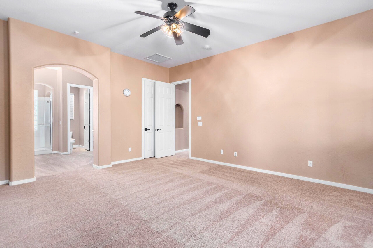 Spacious bedroom in a Palm Valley home, Goodyear, AZ, featuring neutral tones, a ceiling fan, and a private ensuite bathroom. This room offers great potential for high rental revenue, whether used as a master suite or transformed into an additional guest room. Its large size and flexible layout make it ideal for short-term rental opportunities, providing comfort and privacy for potential renters.