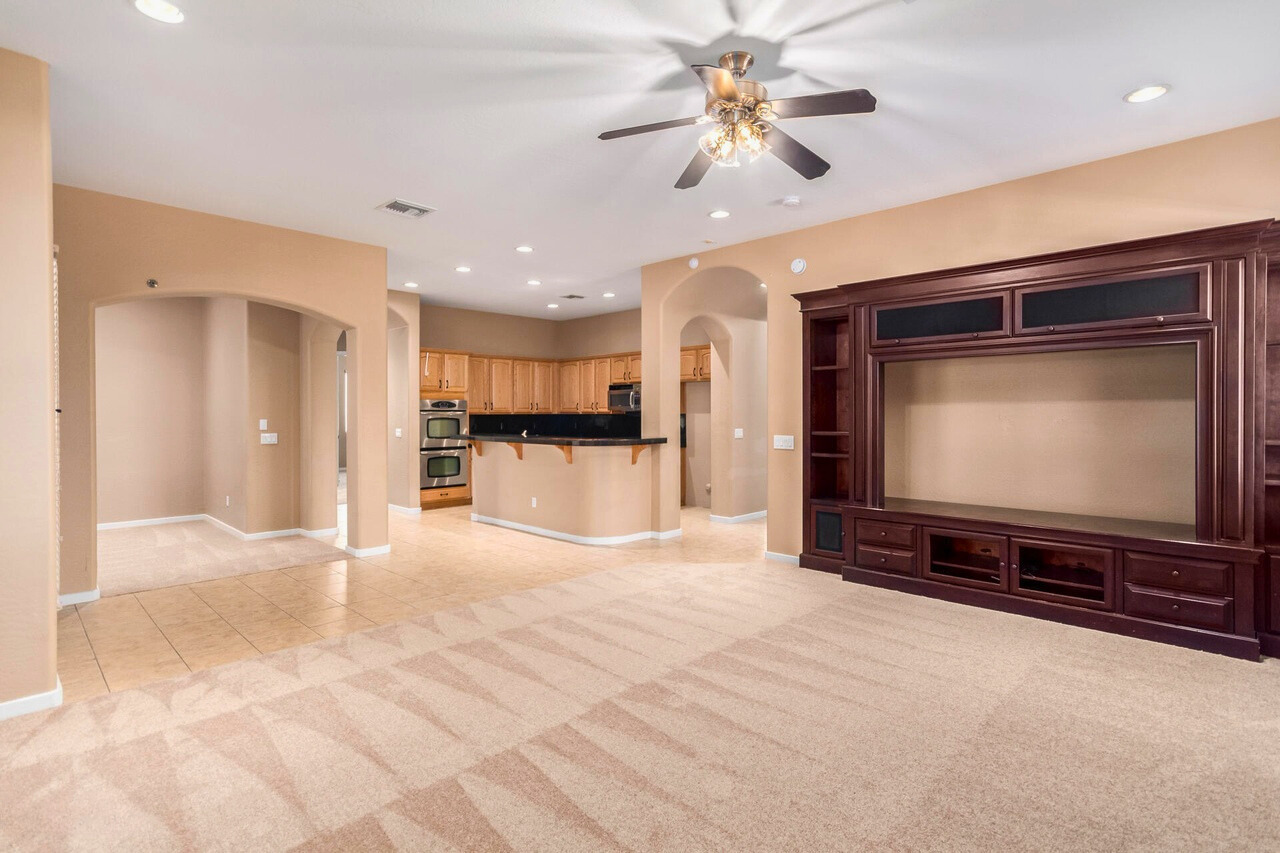 Spacious open-concept living room and kitchen in a Palm Valley home, Goodyear, AZ. Featuring a built-in entertainment center, tile and carpet flooring, recessed lighting, and a ceiling fan. The kitchen includes granite countertops, a breakfast bar, double ovens, and wooden cabinetry, perfect for family gatherings and entertaining. This inviting space offers functionality and comfort in one of Goodyear's most desirable communities.