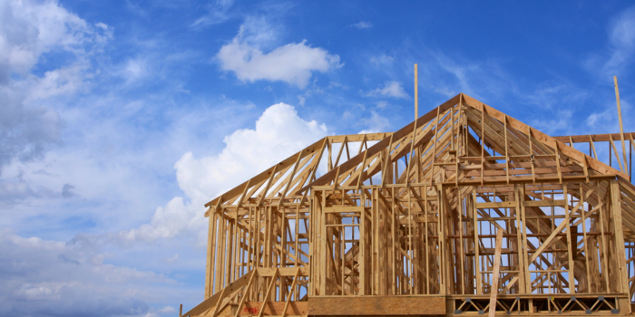 Framed new construction home under a bright blue sky, illustrating the challenges builders will face in 2025 with higher costs due to increased regulations, labor expenses, and material prices. These factors are expected to raise new home prices, making 2024 year-end incentives a prime opportunity for buyers to lock in lower costs before these changes take effect.