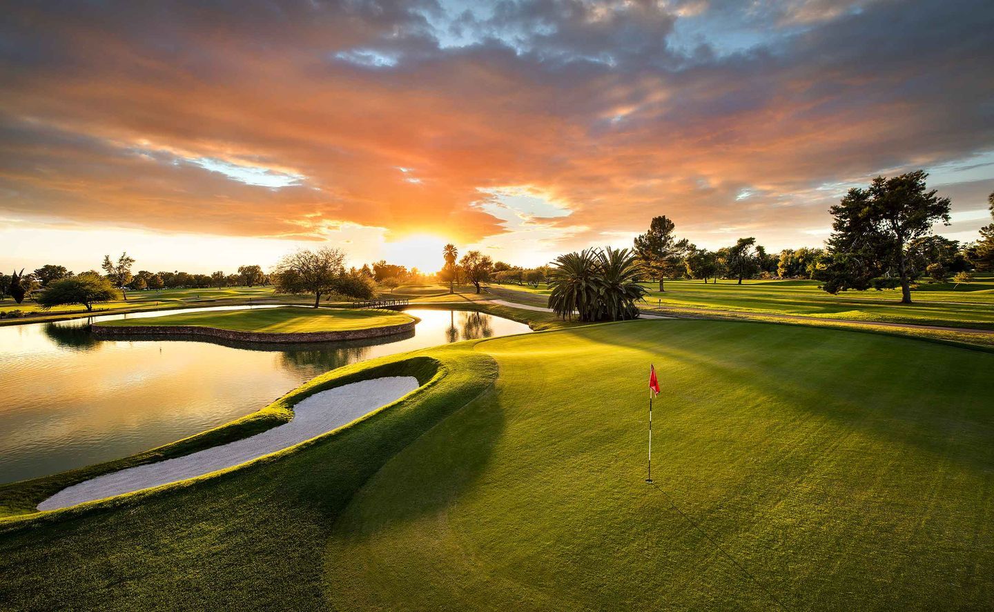 Scenic view of a pristine golf course at sunset in Arizona, featuring lush greenery, tranquil water features, and palm trees, showcasing the state's lifestyle benefits, including outdoor recreation, warm climate, and picturesque landscapes.