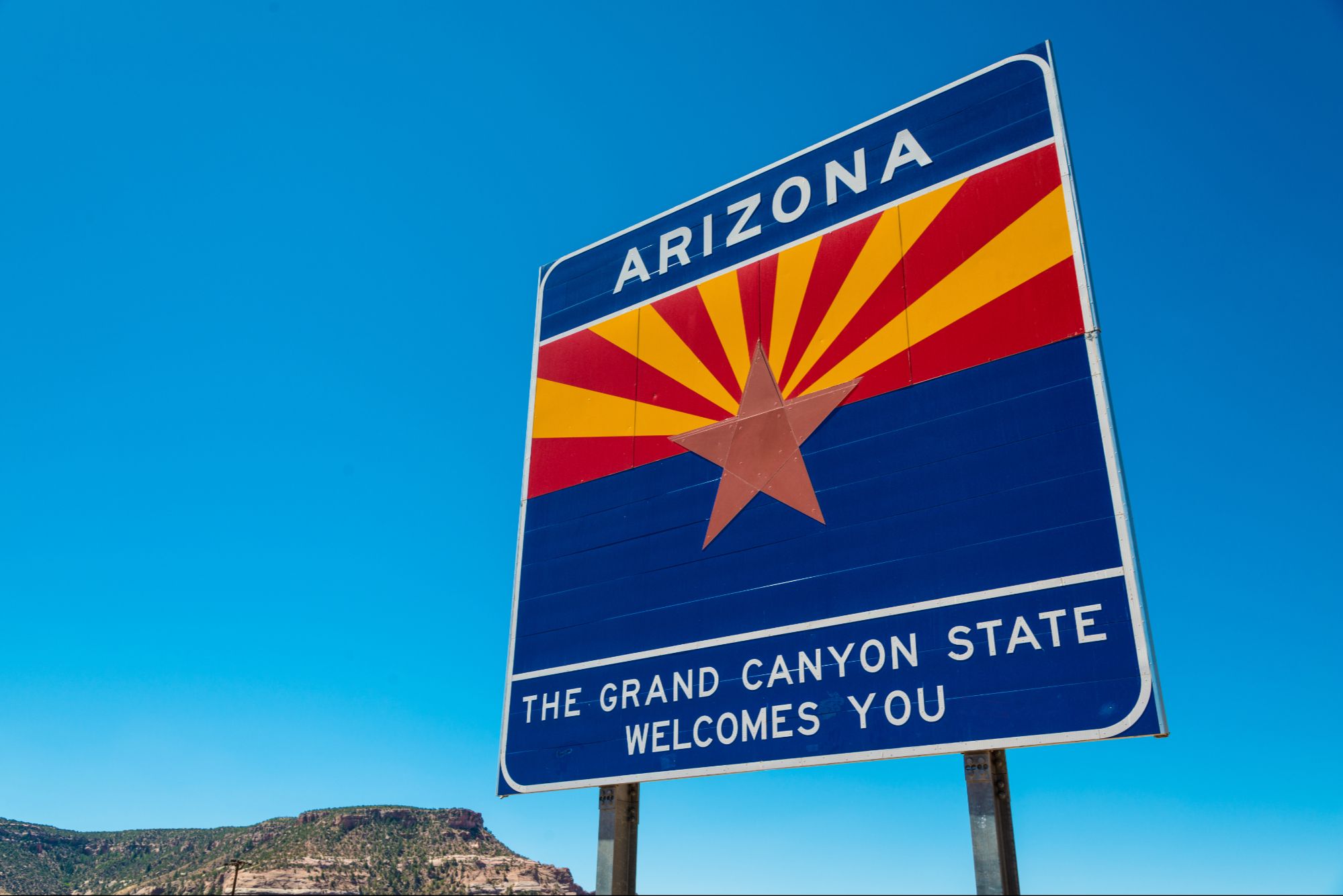 Image of the 'Arizona - The Grand Canyon State Welcomes You' sign against a bright blue sky, emphasizing why Arizona's landlord-friendly rental laws and high demand for rental properties in cities like Scottsdale, Phoenix, and Queen Creek make it an attractive state for property investment. The blog highlights rental income potential, tax benefits, and property appreciation as key advantages for homeowners in Arizona.