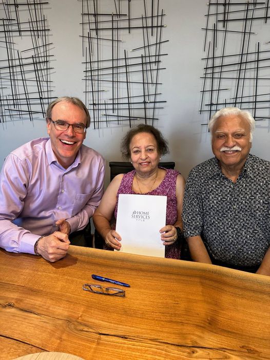 David Campbell sitting next to couple while smiling, the woman in the middle is holding a Home Title folder.