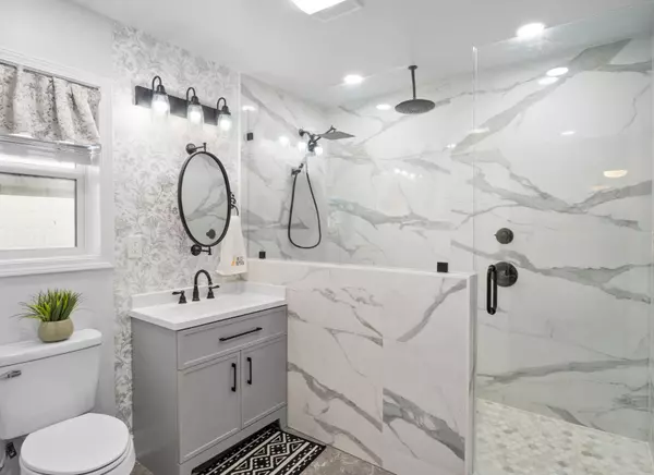 Custom remodeled primary bathroom at 408 Avenue A, Belle Chasse, LA, featuring a marble shower with a rainfall head, a wall-mounted head, and a detachable sprayer.